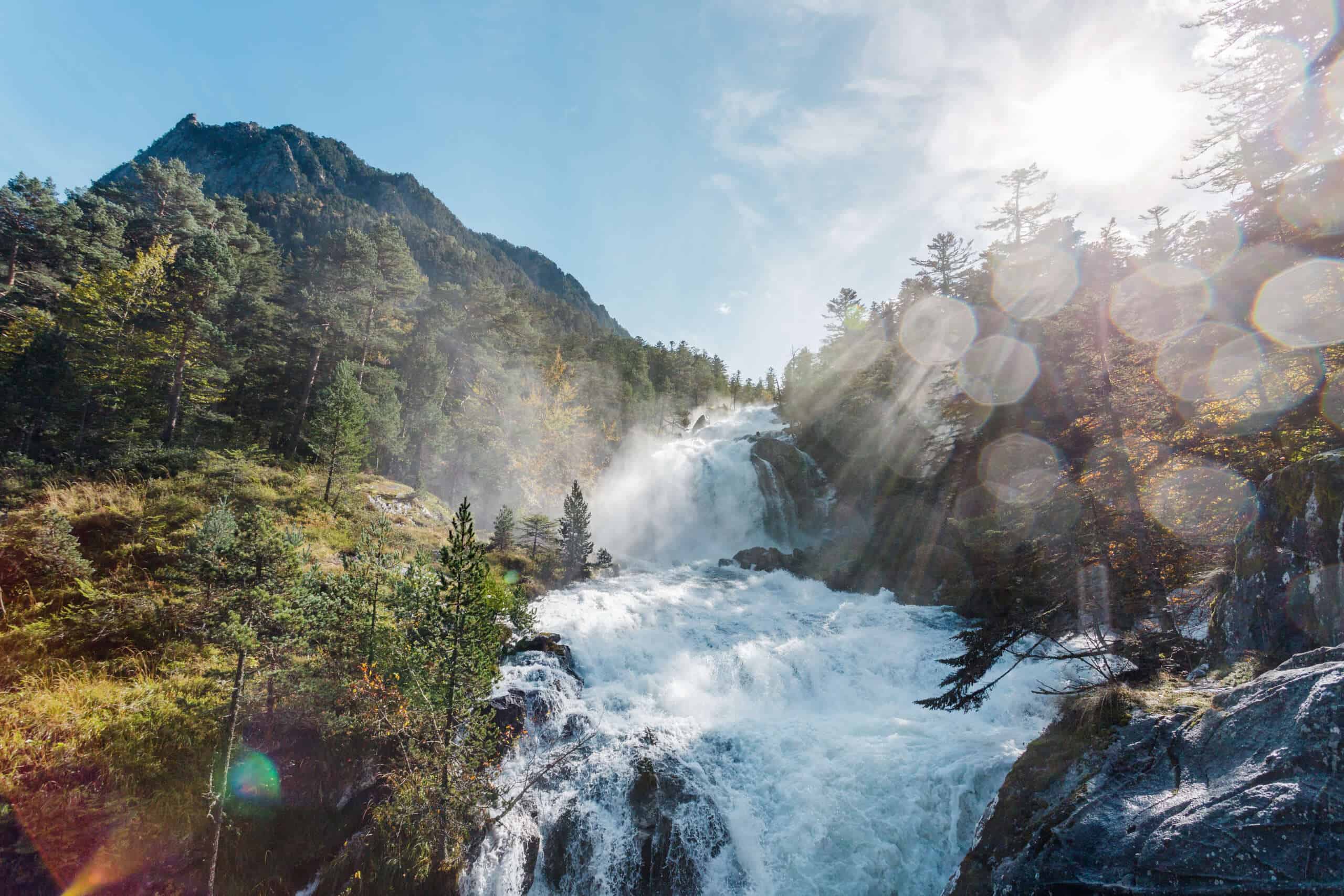 Cascade naturelle en montagne avec forêt et soleil, paysage d'eau vive.